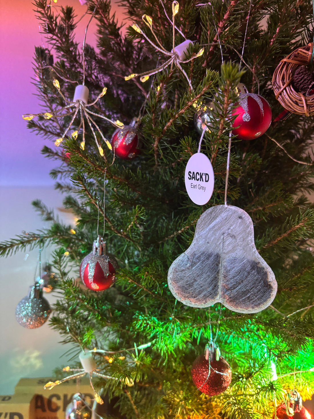 A SACK'D novelty tea bag hanging from a Christmas tree with red ornaments
